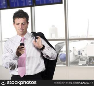 Businessman is waiting for his flight on the airport. He is playing a game or dialing someone on his mobile.