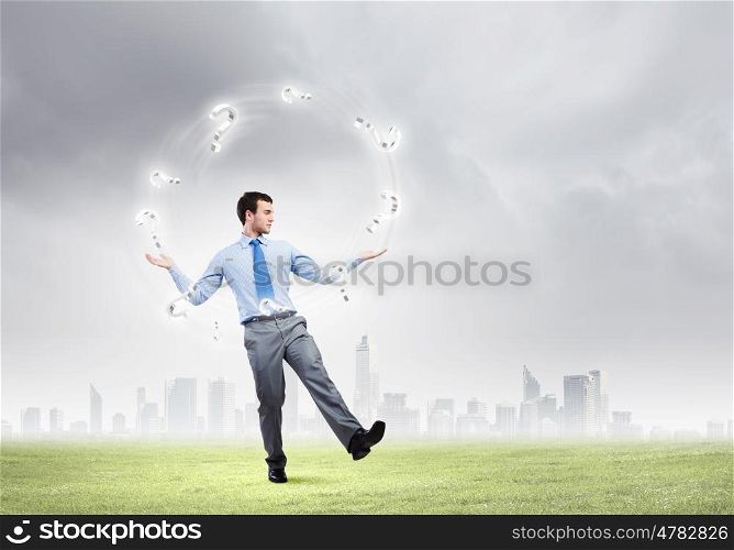 Businessman juggler. Handsome businessman juggling with question marks against city background