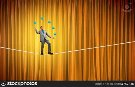 Businessman juggling with balls. Young businessman balancing on rope and juggling with balls
