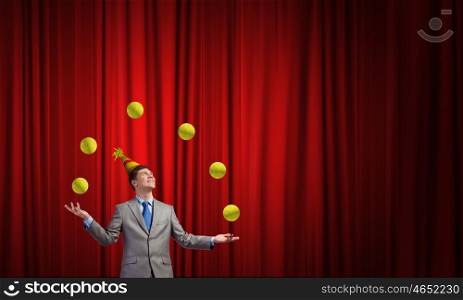 Businessman juggling with balls. Young businessman in cap on stage juggling with balls