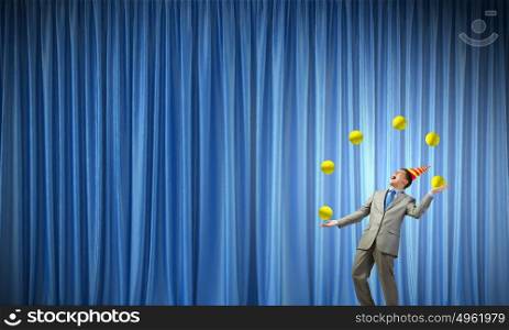 Businessman juggling with balls. Young businessman in cap on stage juggling with balls