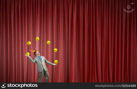 Businessman juggling with balls. Young businessman in cap on stage juggling with balls