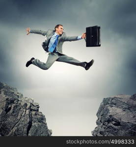 Businessman jumping over gap. Image of young businessman jumping over gap