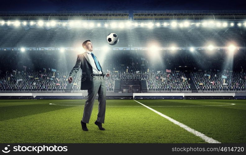 Businessman kicking ball. Young businessman in suit playing football at stadium