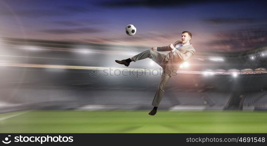 Businessman kicking ball. Young businessman in suit playing football at stadium