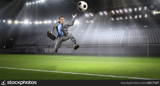 Businessman kicking ball. Young businessman in suit playing football at stadium