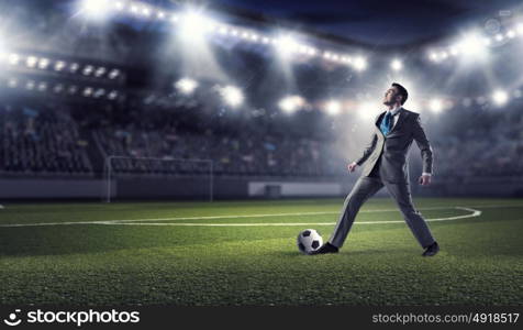 Businessman kicking ball. Young businessman in suit playing football at stadium