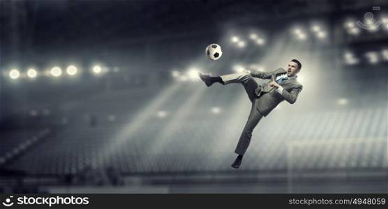 Businessman kicking ball. Young businessman in suit playing football at stadium