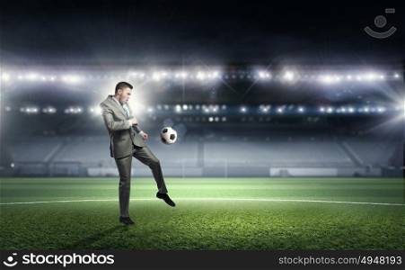 Businessman kicking ball. Young businessman in suit playing football at stadium