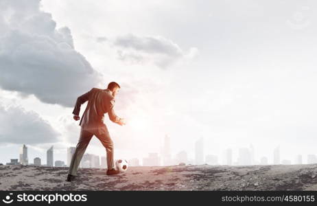 Businessman kicking ball. Young businessman in suit playing football outdoors