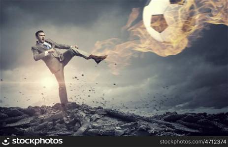 Businessman kicking ball. Young businessman in suit playing football outdoors