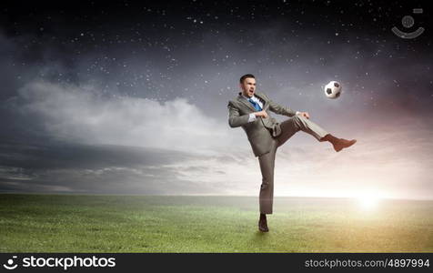 Businessman kicking ball. Young businessman in suit playing football outdoors