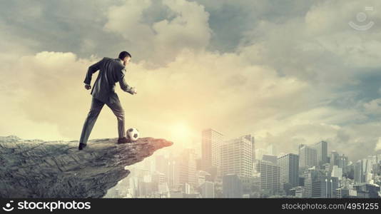 Businessman kicking ball. Young businessman in suit playing football outdoors