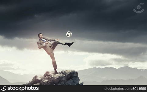 Businessman kicking ball. Young businessman in suit playing football outdoors