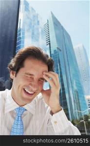Businessman laughing with his head in his hand in front of office buildings