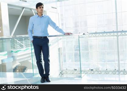 Businessman leaning on balcony railings. Successful and confident businessman in modern building interior