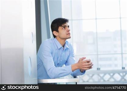 Businessman leaning on balcony railings. Successful and confident businessman with coffee cup in modern building interior