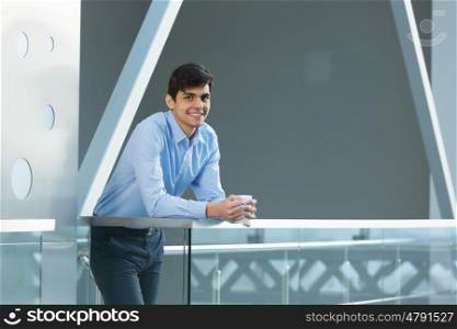 Businessman leaning on balcony railings. Successful and confident businessman with coffee cup in modern building interior