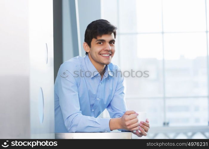 Businessman leaning on balcony railings. Successful and confident businessman with coffee cup in modern building interior