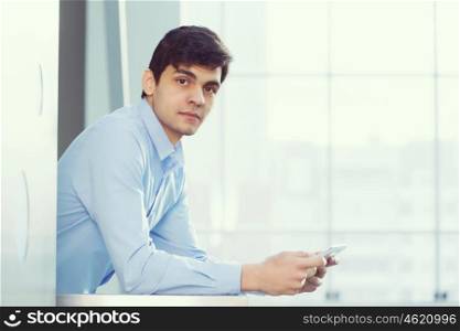 Businessman leaning on balcony railings. Successful and confident businessman with tablet in modern building interior