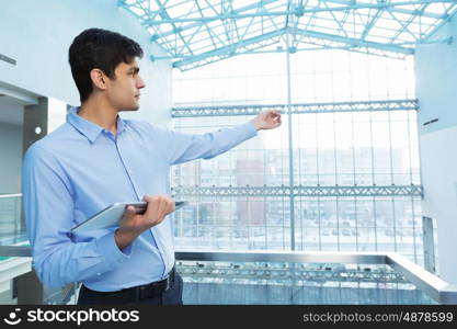 Businessman leaning on balcony railings. Successful and confident businessman with tablet in modern building interior