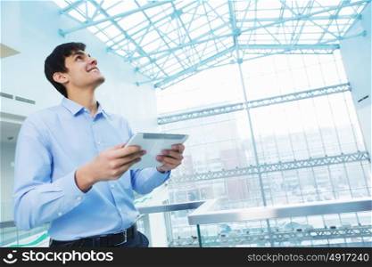Businessman leaning on balcony railings. Successful and confident businessman with tablet in modern building interior