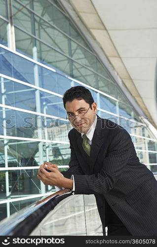 Businessman leaning on railing outside office building