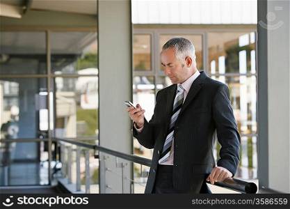 Businessman leaning on railing using mobile phone.