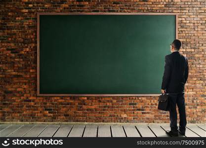 Businessman looking and thinking front of a brick wall with empty chalkboard .