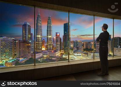Businessman looking and thinking front of a window office with modern city skyline . Evening scene .