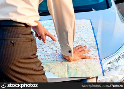 Businessman looking at a map spread out on the hood of a car