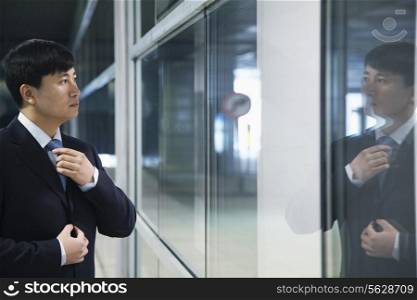 Businessman looking at his reflection and adjusting his tie