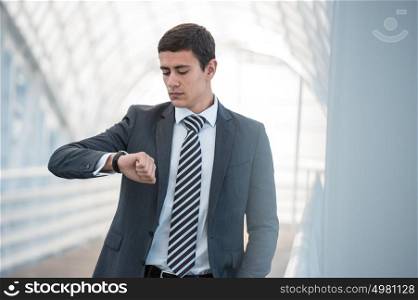 Businessman looking at watches while walking outside modern building