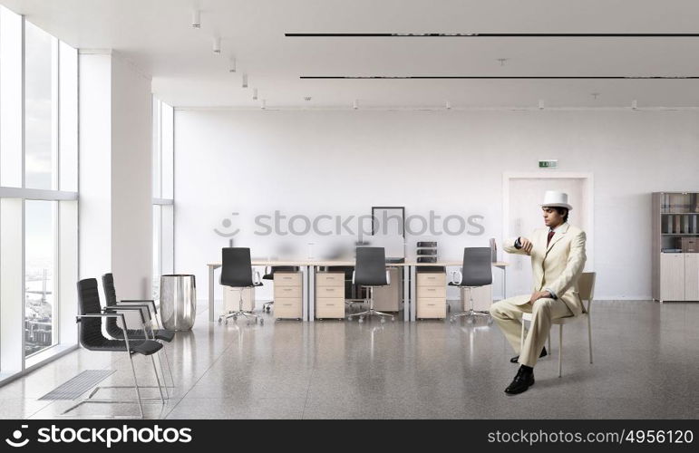 Businessman looking at wristwatch. Elegant businessman in white suit sitting on chair in office interior