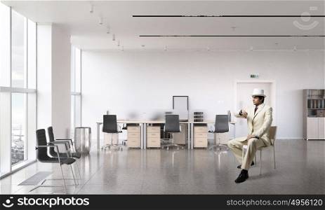 Businessman looking at wristwatch. Elegant businessman in white suit sitting on chair in office interior