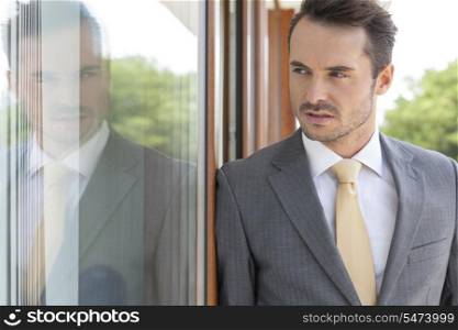Businessman looking away while leaning on glass door