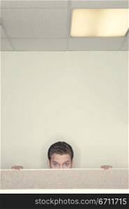 Businessman looking over the cubical wall staring forward with his hands on the top of the cubical wall