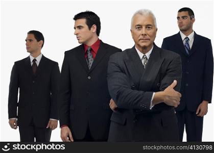 Businessman looking serious with three businessmen standing behind him and looking away