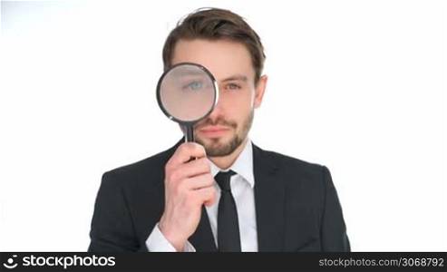 Businessman looking through a magnifying glass enlarging one eye, conceptual of research, investigation, analysis and information, isolated on white