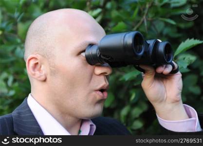 Businessman looking through binoculars. green city park