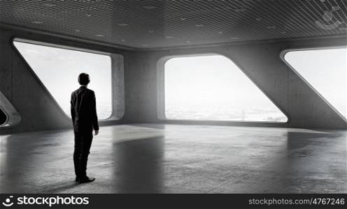 Businessman looking through the window. Businessman in modern building interior standing with back