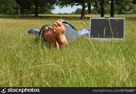 Businessman lying in the grass with a laptop beside him