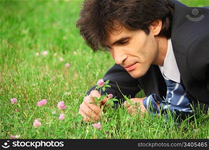 businessman lying on grass looks at clover flower