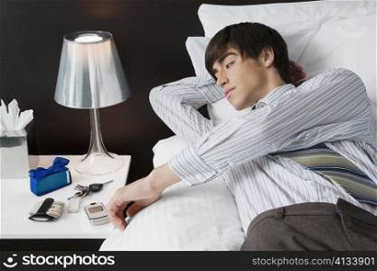 Businessman lying on the bed and looking at a mobile phone