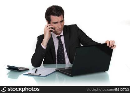 Businessman making call whilst reading from computer screen