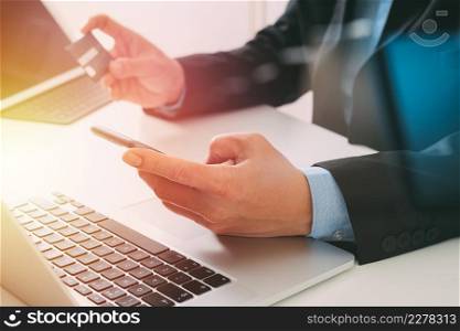 businessman making credit card purchase online with mobile phone and laptop computer on modern desk