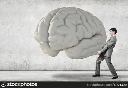 Businessman making effort to carry huge human brain. Great mind