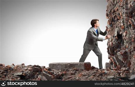 Businessman making effort to move stone wall. Overcoming difficulties