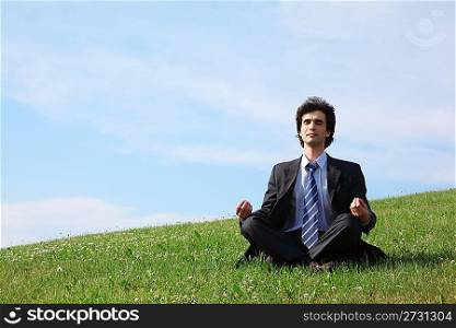 businessman meditates sitting on meadow