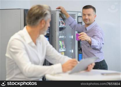 businessman offering colleague a drink from vending machine